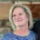Smiling woman with blonde hair wearing a blue patterned top, against a rustic background. — Ellen Bishop obituary