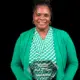 Pamela McDaniel smiling while holding an award, wearing a green cardigan and patterned top.