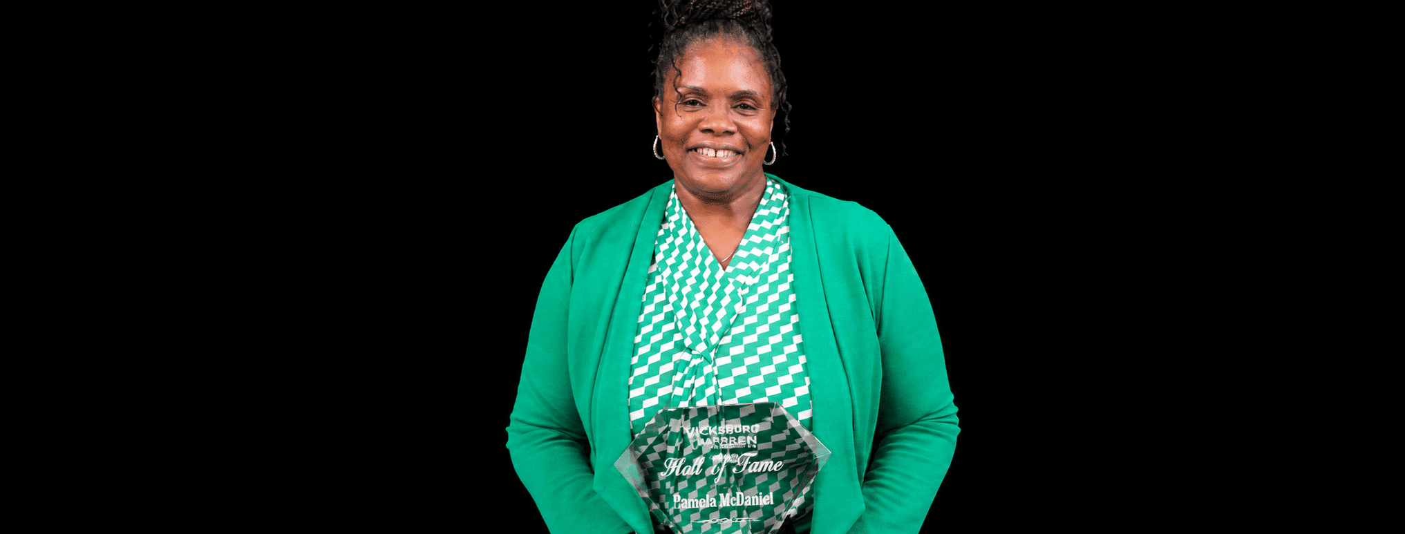 Pamela McDaniel smiling while holding an award, wearing a green cardigan and patterned top.