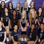 St. Aloysius Lady Flashes volleyball team poses together in their uniforms against a purple backdrop, celebrati — district