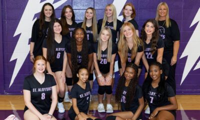 St. Aloysius Lady Flashes volleyball team poses together in their uniforms against a purple backdrop, celebrati — district