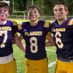 Three St. Aloysius Junior High football players celebrating after a game, wearing purple and gold uniforms, with a — 42-8