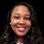 Smiling woman with curly hair wearing a black blazer and pearl necklace, representing Dr. Danielle Nelson.