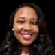 Smiling woman with curly hair wearing a black blazer and pearl necklace, representing Dr. Danielle Nelson.