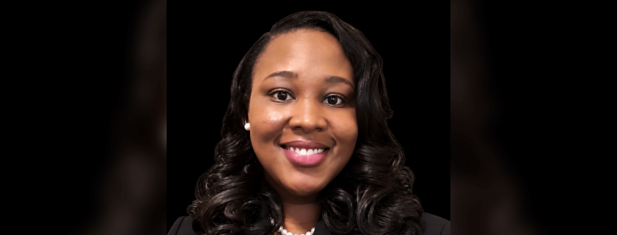 Smiling woman with curly hair wearing a black blazer and pearl necklace, representing Dr. Danielle Nelson.