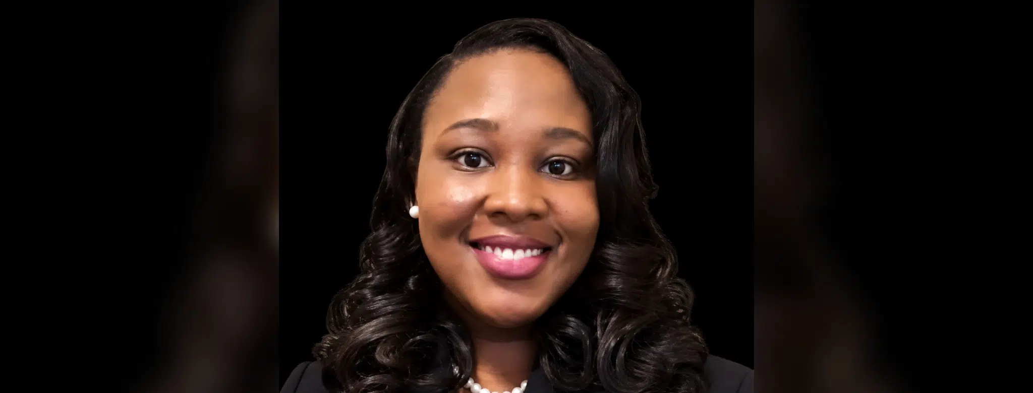 Smiling woman with curly hair wearing a black blazer and pearl necklace, representing Dr. Danielle Nelson.