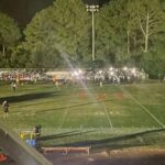 Football field at night with stadium lights out, players and spectators gathered in darkness during a suspended game.