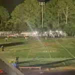 Football field at night with stadium lights out, players and spectators gathered in darkness during a suspended game.