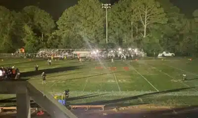 Football field at night with stadium lights out, players and spectators gathered in darkness during a suspended game.