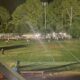 Football field at night with stadium lights out, players and spectators gathered in darkness during a suspended game.