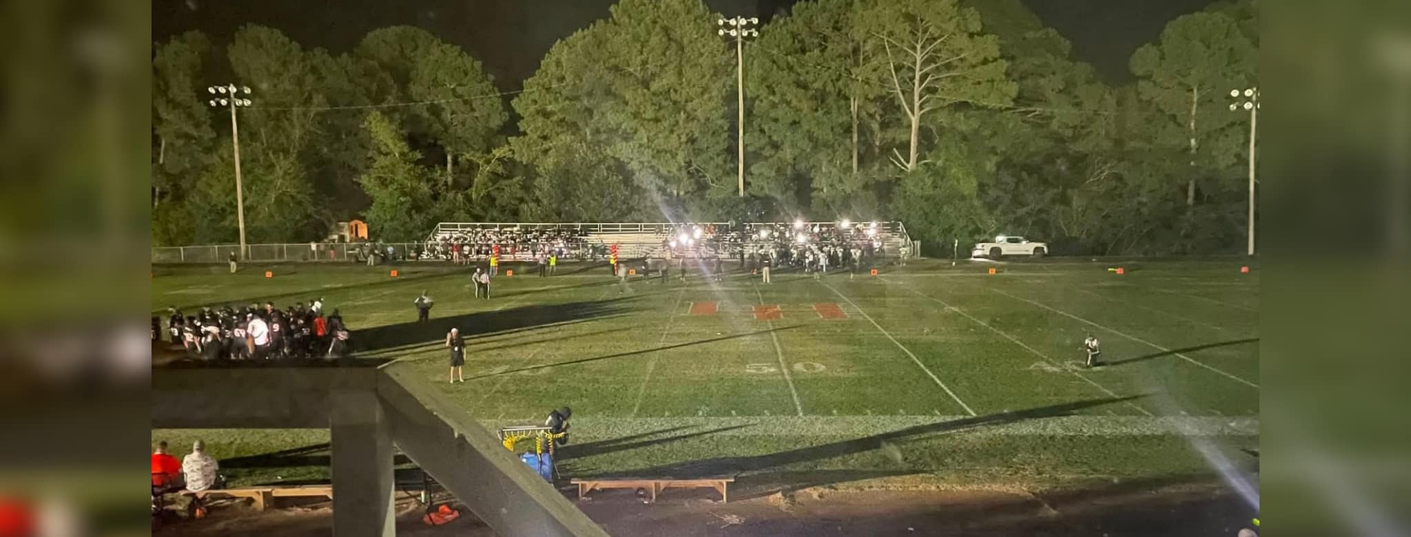 Football field at night with stadium lights out, players and spectators gathered in darkness during a suspended game.