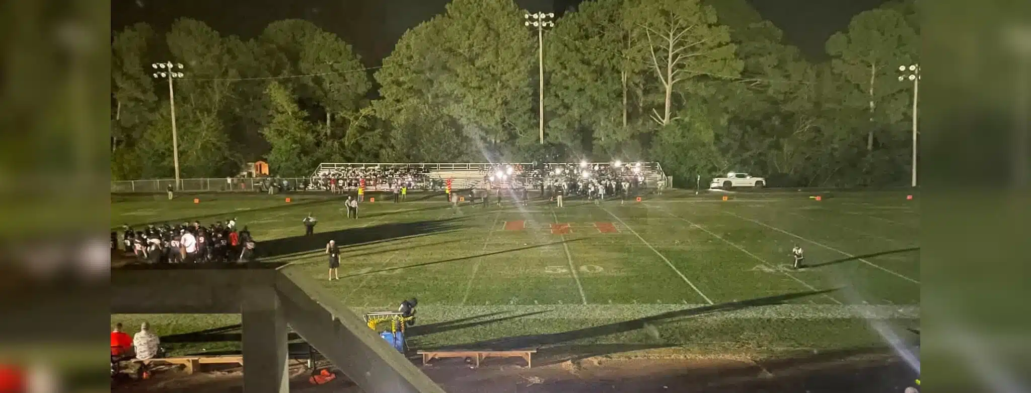 Football field at night with stadium lights out, players and spectators gathered in darkness during a suspended game.