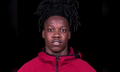 Michael Hall, a young athlete with long dark hair, wearing a red jacket, looking directly at the camera.
