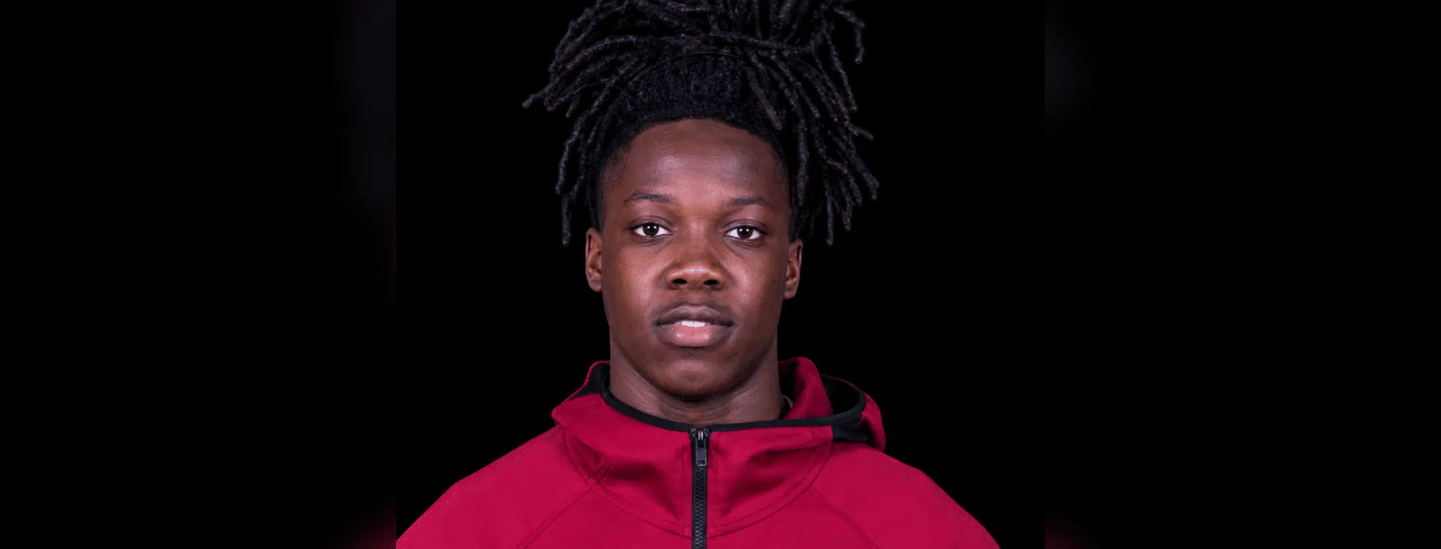 Michael Hall, a young athlete with long dark hair, wearing a red jacket, looking directly at the camera.