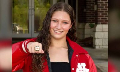 A swimmer in a red jacket proudly displays a championship ring, smiling at the camera. — Splash 4 Gold Meet