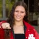 A swimmer in a red jacket proudly displays a championship ring, smiling at the camera. — Splash 4 Gold Meet