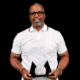 Kevin Dent holding an award, smiling, wearing a white polo shirt with glasses.