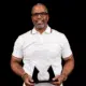 Kevin Dent holding an award, smiling, wearing a white polo shirt with glasses.
