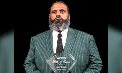 Andre Bennett holding a Hall of Fame plaque, wearing a green striped suit and tie, with a serious expression.