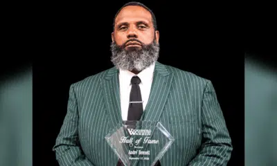 Andre Bennett holding a Hall of Fame plaque, wearing a green striped suit and tie, with a serious expression.