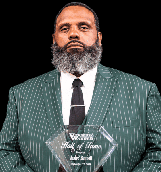 Andre Bennett holding a Hall of Fame plaque, wearing a green striped suit and tie, with a serious expression.