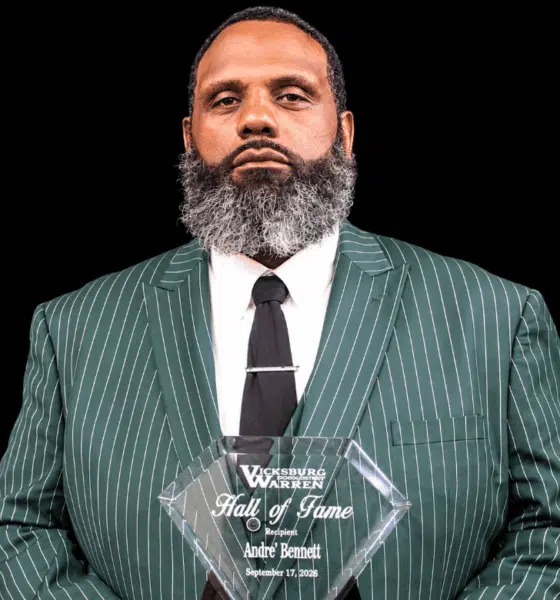 Andre Bennett holding a Hall of Fame plaque, wearing a green striped suit and tie, with a serious expression.