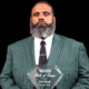 Andre Bennett holding a Hall of Fame plaque, wearing a green striped suit and tie, with a serious expression.