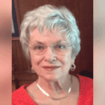 A smiling elderly woman with short gray hair and glasses, wearing a red top, exuding warmth a — Patricia Fairchild Oglesby