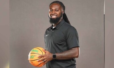 DeAndre King, a basketball coach, smiles while holding a basketball in a black polo shirt.