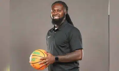 DeAndre King, a basketball coach, smiles while holding a basketball in a black polo shirt.