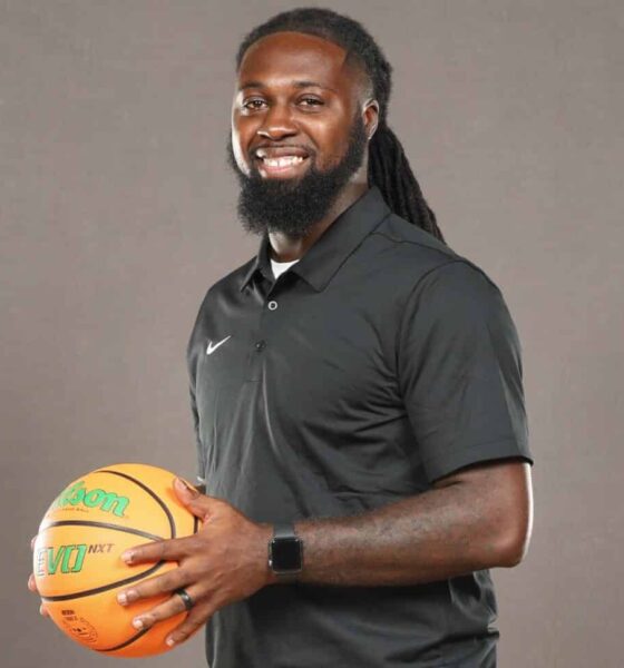 DeAndre King, a basketball coach, smiles while holding a basketball in a black polo shirt.