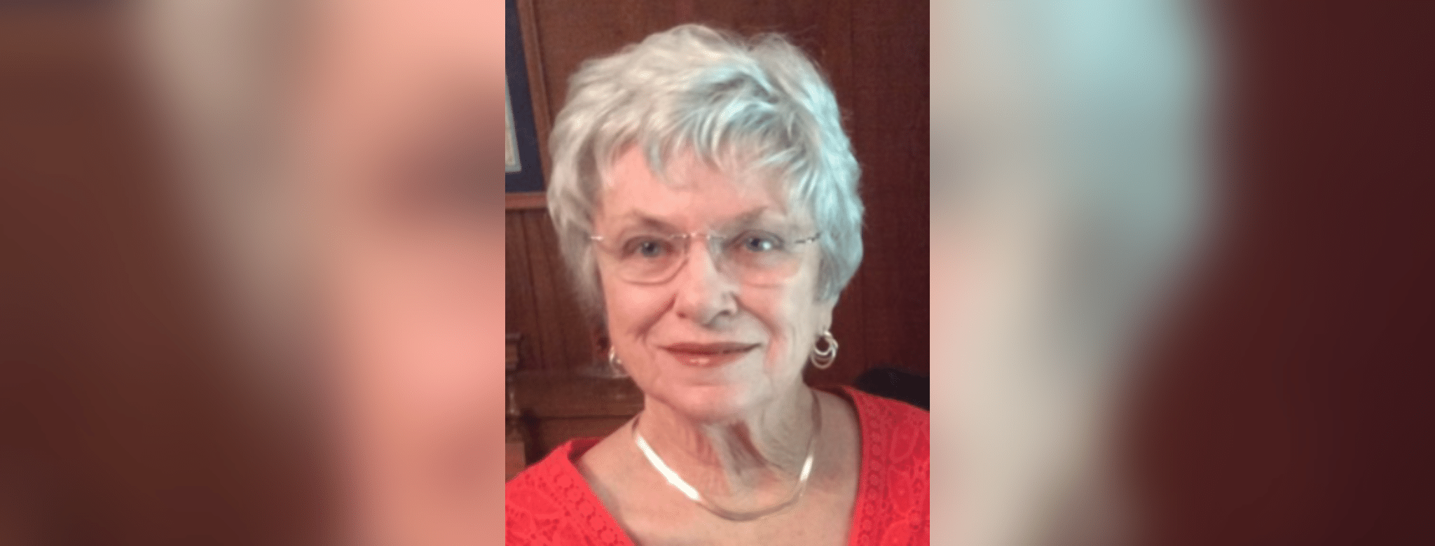 A smiling elderly woman with short gray hair and glasses, wearing a red top, exuding warmth a — Patricia Fairchild Oglesby