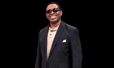 Smiling man in sunglasses and a black suit, standing confidently against a dark background. — Cleothia Williams
