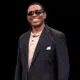 Smiling man in sunglasses and a black suit, standing confidently against a dark background. — Cleothia Williams