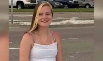 A young woman with long blonde hair smiles while sitting outdoors, wearing a white tank top. — Avery Read Carroll