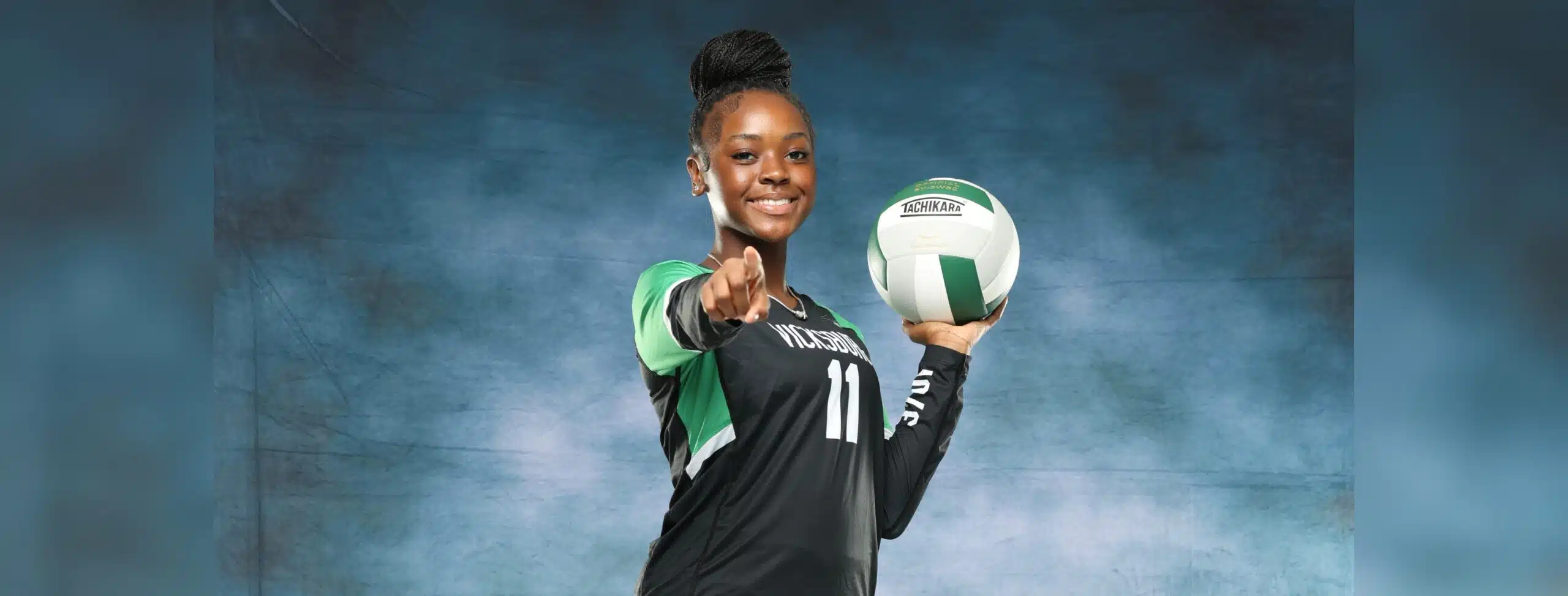 A volleyball player in a black uniform holds a volleyball and points confidently at the camera, sho — Vicksburg volleyball