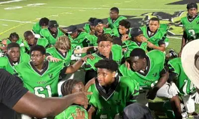 Vicksburg Junior High football team in green jerseys huddled together on the field after a game. — Undefeated