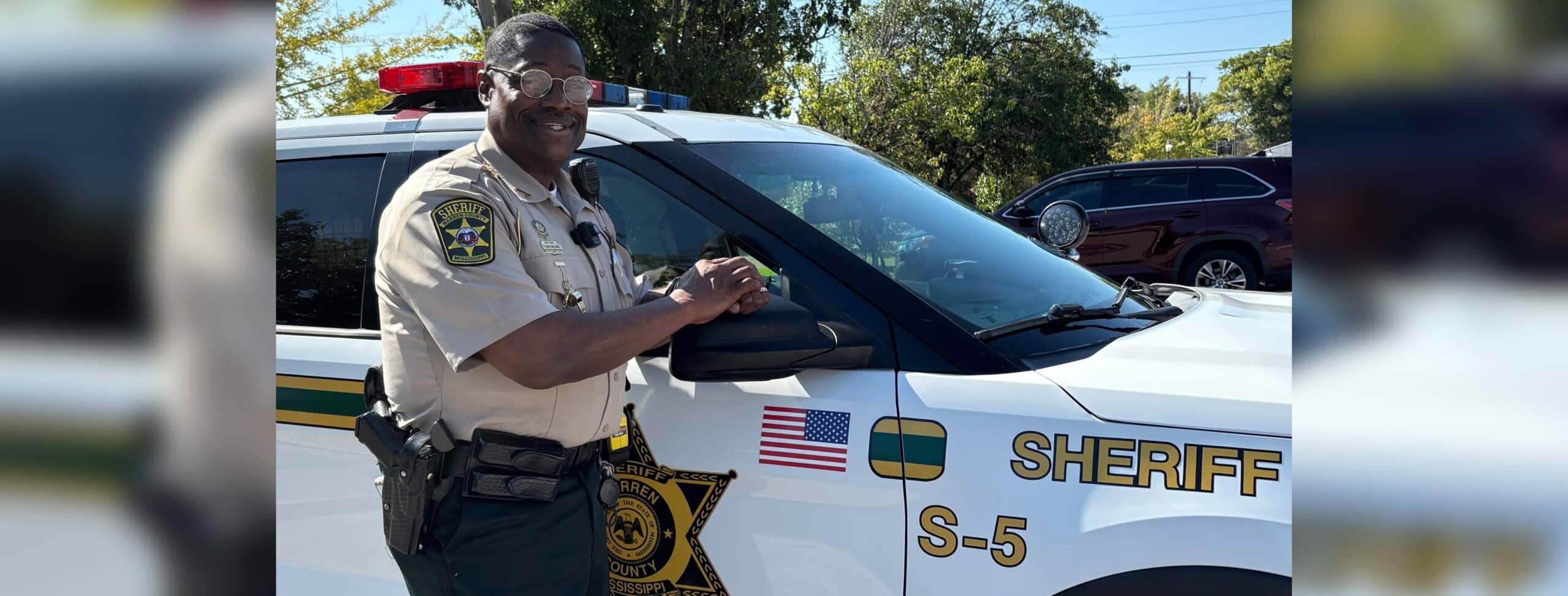 John Williams, Deputy of the Year, stands next to a sheriff's vehicle, smiling and posing for the camera.
