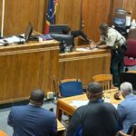 A courtroom scene with a judge, a sheriff's deputy, and several individuals seated at a table, discussing — Second chance