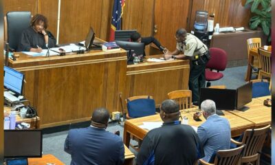 A courtroom scene with a judge, a sheriff's deputy, and several individuals seated at a table, discussing — Second chance