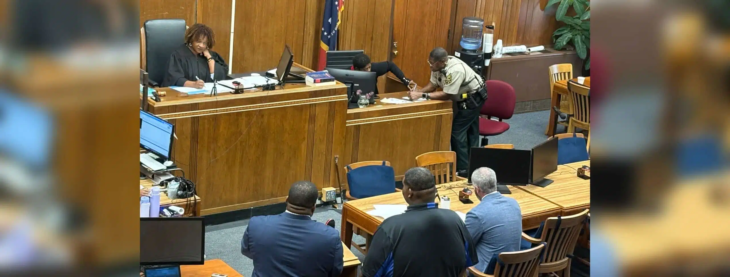 A courtroom scene with a judge, a sheriff's deputy, and several individuals seated at a table, discussing — Second chance
