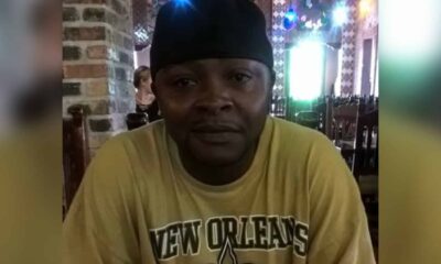 A man wearing a yellow New Orleans Saints t-shirt sits indoors, smiling softly. — Alan Fredrick Lyons jr