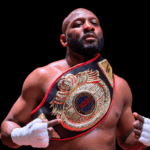 Martin Trey Brown, a muscular fighter, poses confidently with a championship belt in a boxing ring, showcasing his MMA suc…