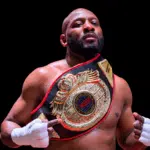 Martin Trey Brown, a muscular fighter, poses confidently with a championship belt in a boxing ring, showcasing his MMA suc…