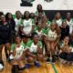Vicksburg High School volleyball team poses together in their gym after a match, celebrating their victory.