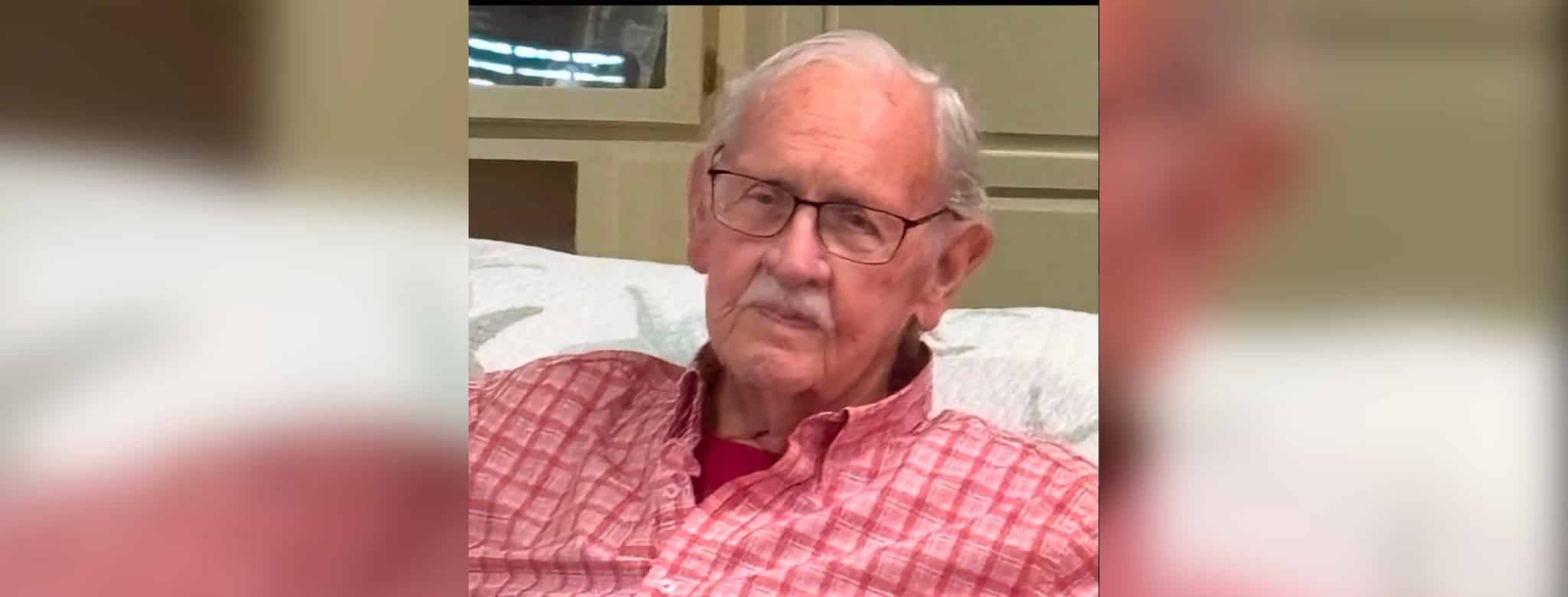 Elderly man with glasses and a pink checkered shirt sitting on a couch, looking thoughtfully at th — James Douglas Burnett