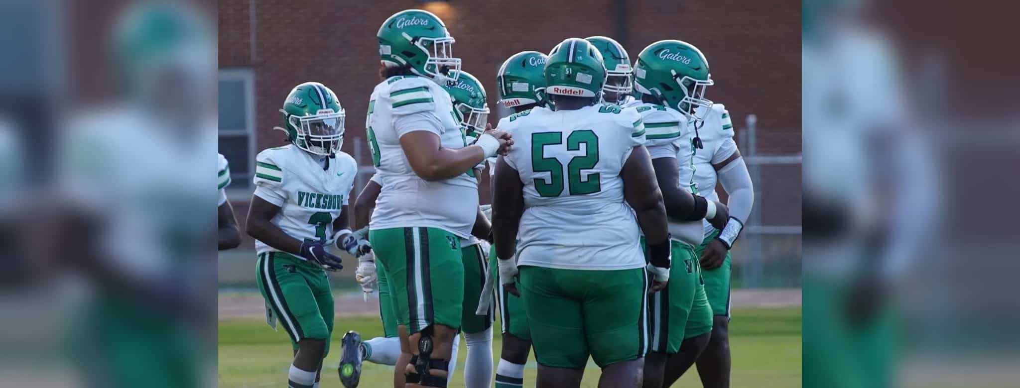 Vicksburg High School football players in green and white uniforms huddle on the — VHS fell short 34-24 against Ridgeland