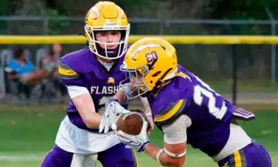 Two football players in purple and yellow uniforms executing a handoff during a — Flashes fall to Riverfield in close game