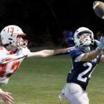 A football player in a blue jersey reaches for the ball while an opponent in a red jersey attempts to defend. — 58-32