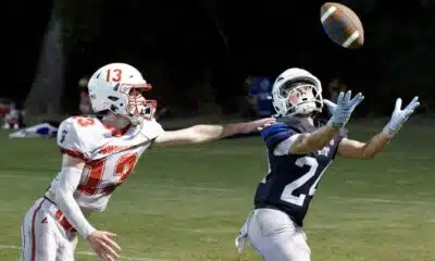 A football player in a blue jersey reaches for the ball while an opponent in a red jersey attempts to defend. — 58-32